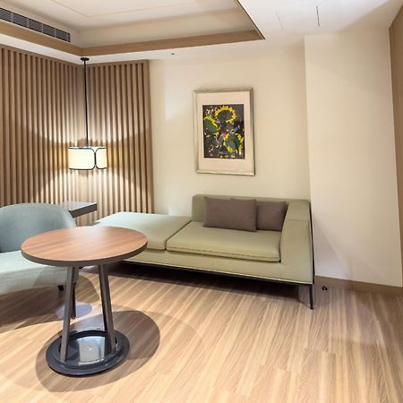Caesar Metro Taipei Hotel Luaran gambar The photo shows a cozy interior space, likely a hotel room or a living area. On the left side, there’s a light green sofa with two pillows and a small round table in front of it. To the left of the sofa, there's a stylish chair. A piece of artwork is