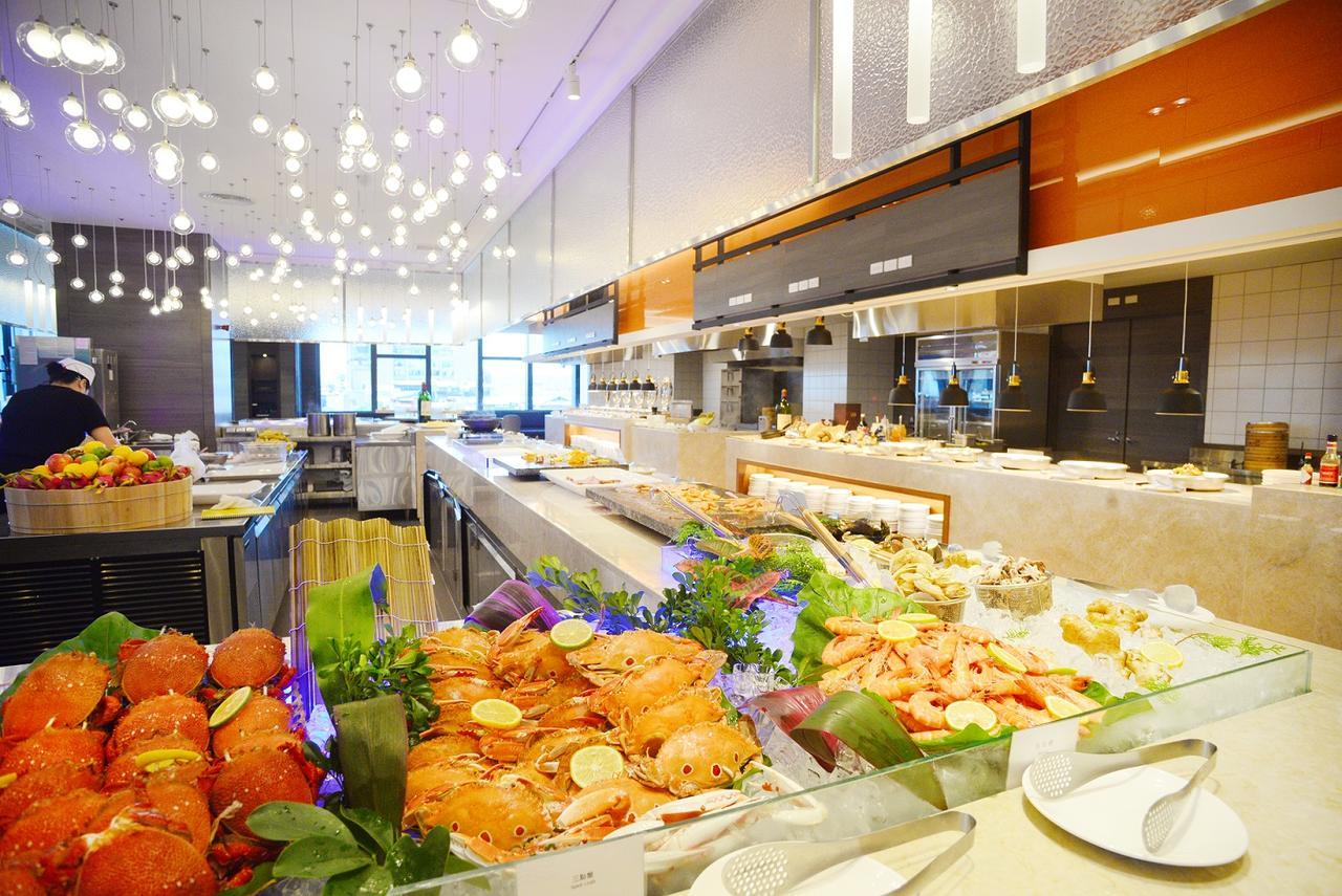 Caesar Metro Taipei Hotel Luaran gambar The photo shows a modern dining area, likely a buffet restaurant. In the foreground, there is a display of seafood, including various types of crabs, shrimp, and other shellfish, garnished with lemon slices and greenery. Behind this seafood display, 