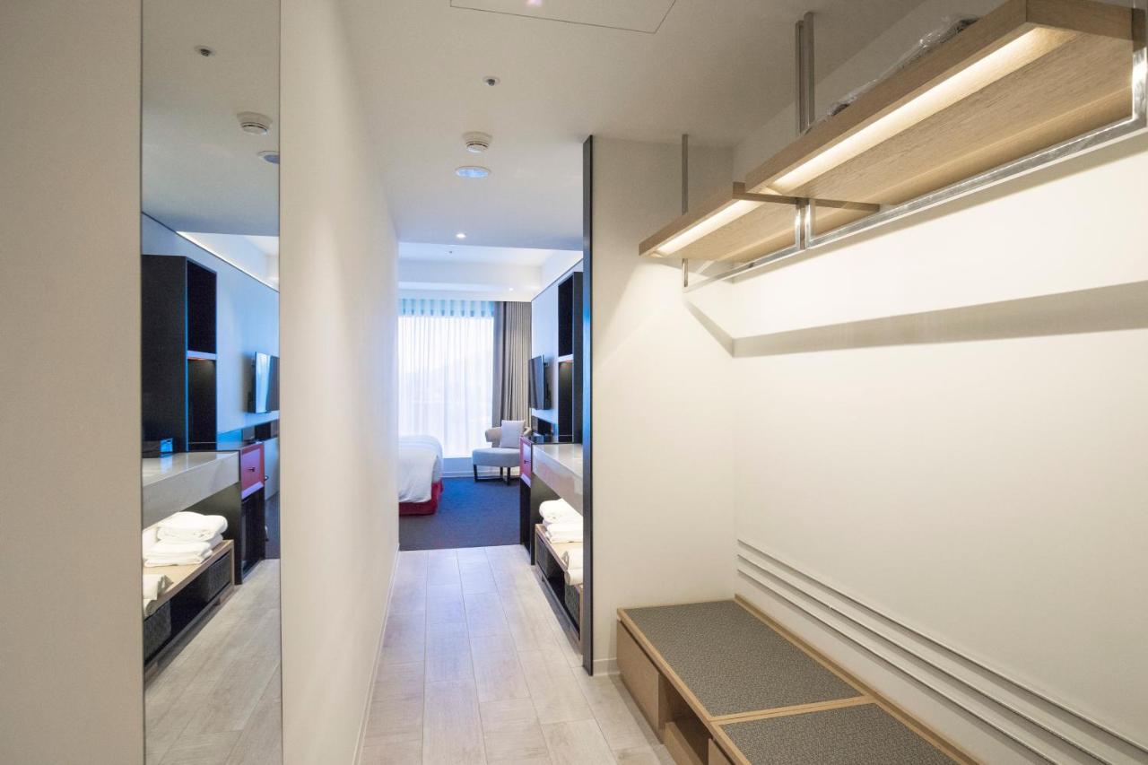 Caesar Metro Taipei Hotel Luaran gambar The photo shows a modern hotel room corridor. On one side, there's a small area with shelving and a bench. The opposite side features dark cabinetry and a large mirror. In the background, light filters in through a window with drapes, revealing a gli