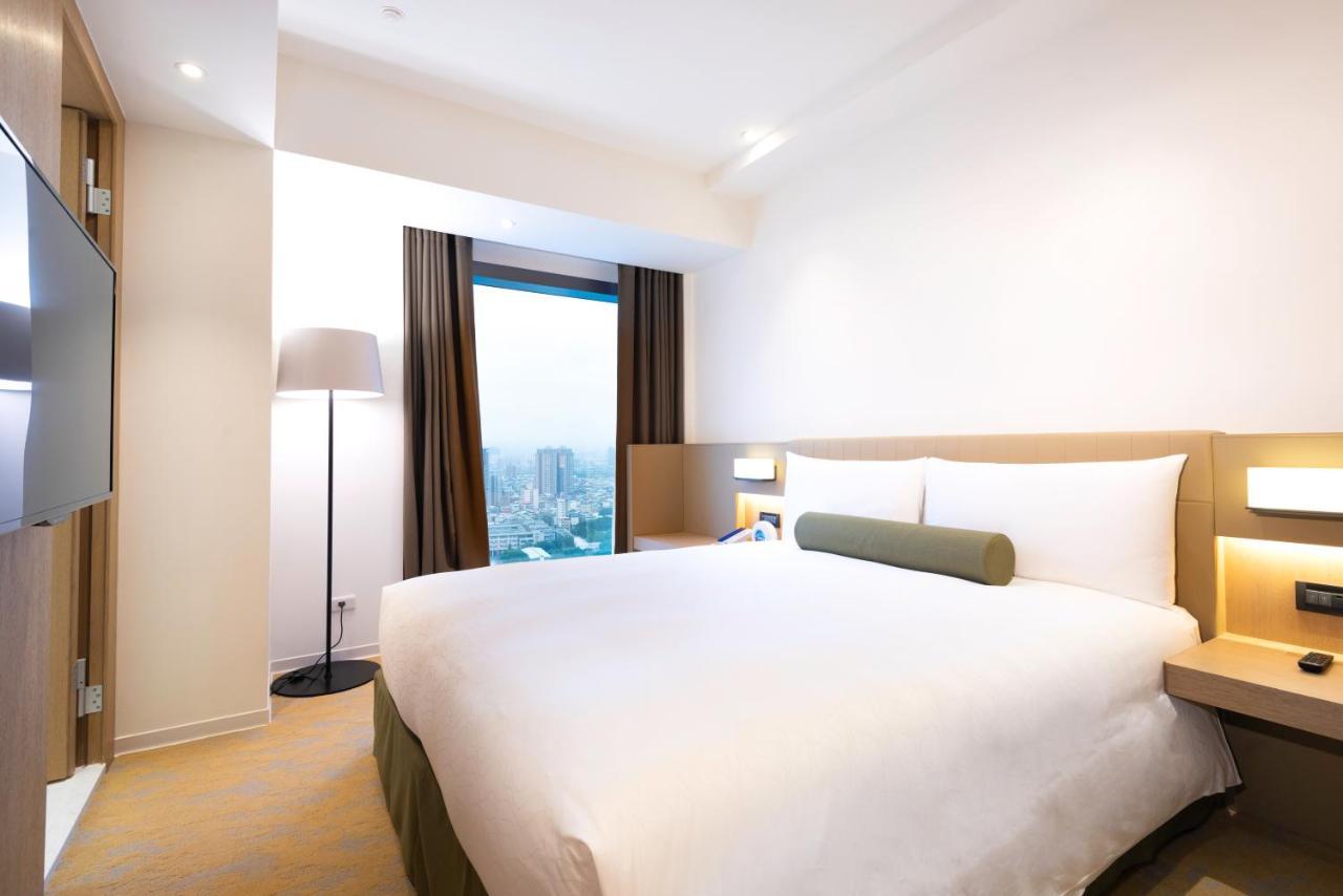 Caesar Metro Taipei Hotel Luaran gambar The photo shows a modern hotel room with a simple and clean design. It features a double bed with white bedding and a green accent pillow. There are two large windows with dark curtains, allowing natural light to enter. A floor lamp stands beside the