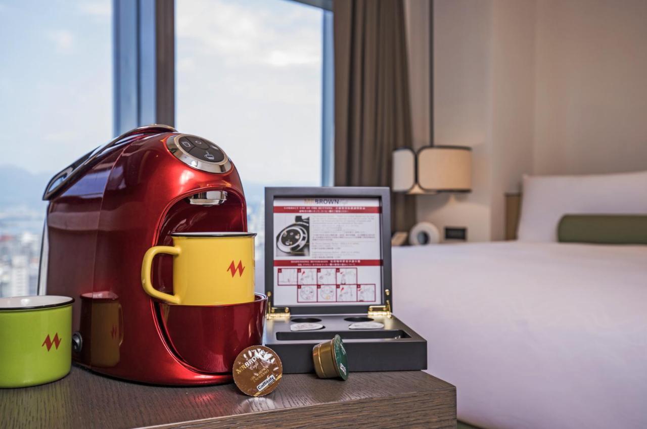 Caesar Metro Taipei Hotel Luaran gambar The image shows a cozy hotel room setting featuring a red coffee maker on a wooden table. Next to the coffee maker are two yellow mugs and a brown capsule, likely used for coffee. There is also a box containing a selection of coffee capsules. In the 