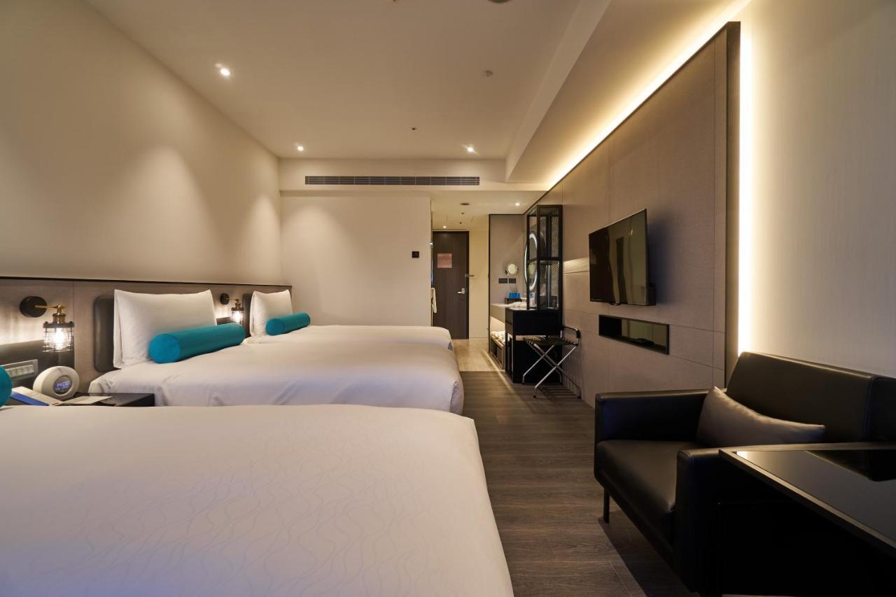 Caesar Metro Taipei Hotel Luaran gambar The photo displays a modern hotel room featuring two beds with white linens and turquoise accent pillows. There's a sleek black chair positioned next to one of the beds. A flat-screen TV is mounted on the wall opposite the beds, and there's a stylish