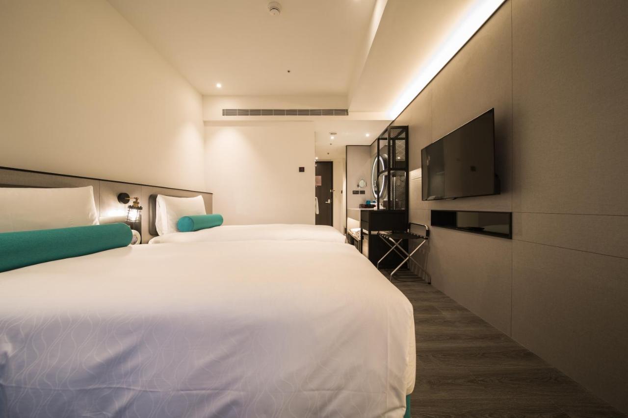 Caesar Metro Taipei Hotel Luaran gambar The photo shows a modern hotel room featuring two beds with white linens and teal accents. The walls are a light, neutral color, contributing to a clean and contemporary aesthetic. There is a minimalist design, with a mounted flat-screen TV on one wa