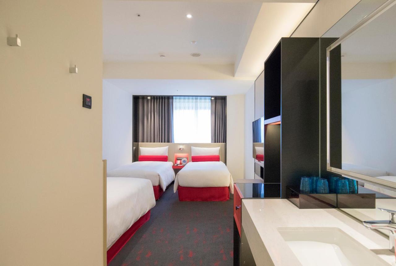 Caesar Metro Taipei Hotel Luaran gambar The photo shows the interior of a hotel room. It features two single beds with white linens and red accents. There is a window with sheer curtains allowing natural light to enter the room. The floor is carpeted, and the decor is modern and minimalist